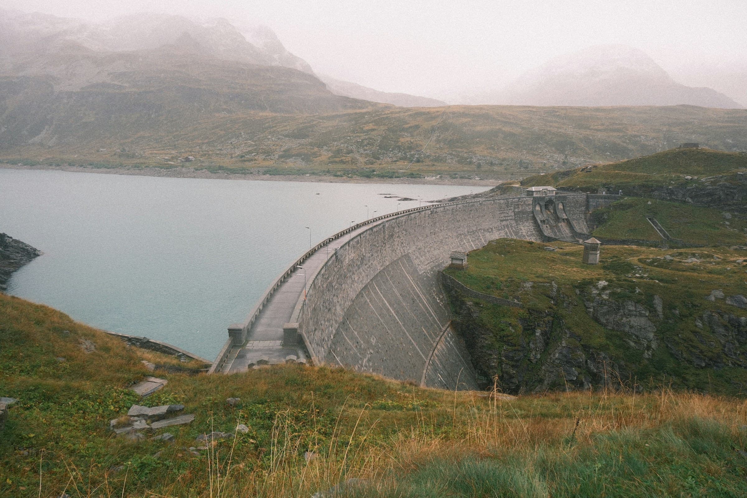 Curved concrete dam holding back a large lake — permanent infrastructure storing value behind a deliberate structural choice